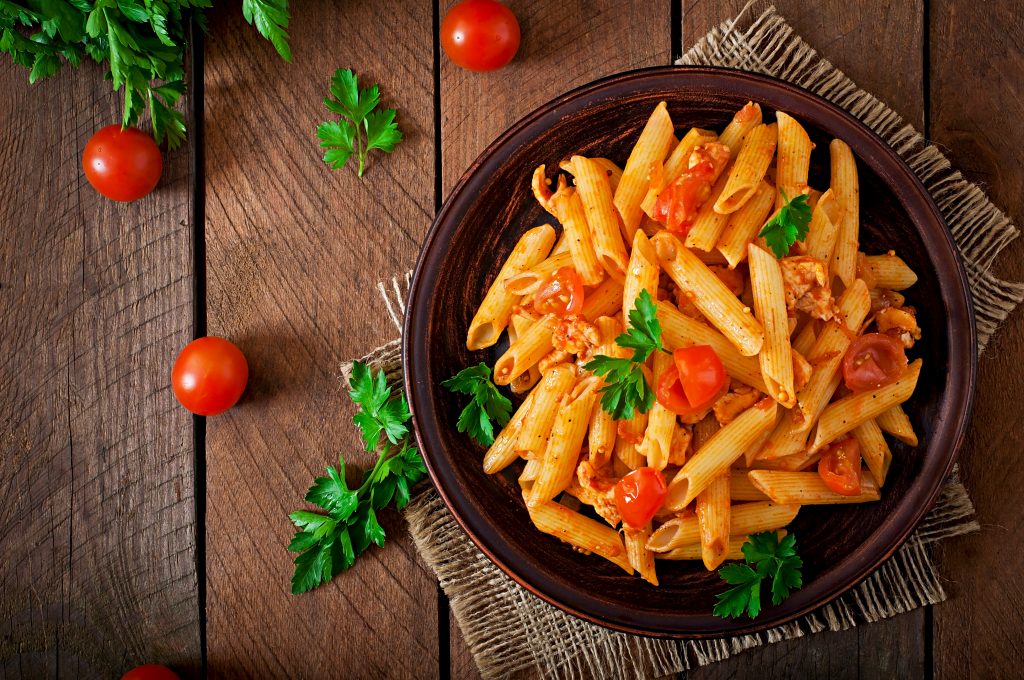 Penne pasta in tomato sauce with chicken and tomatoes on a wooden table